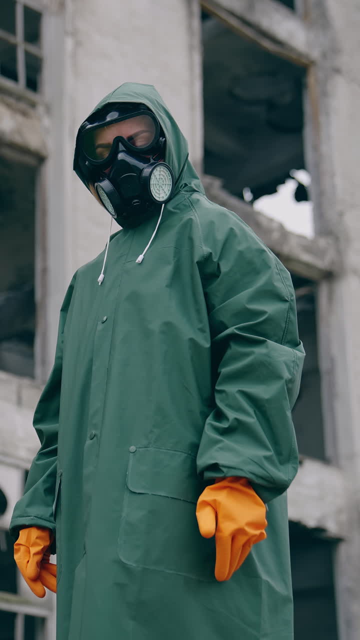 Man in protective clothing and a gas mask is standing on the background of ruined building. The concept of a post-apocalyptic world. Vertical video