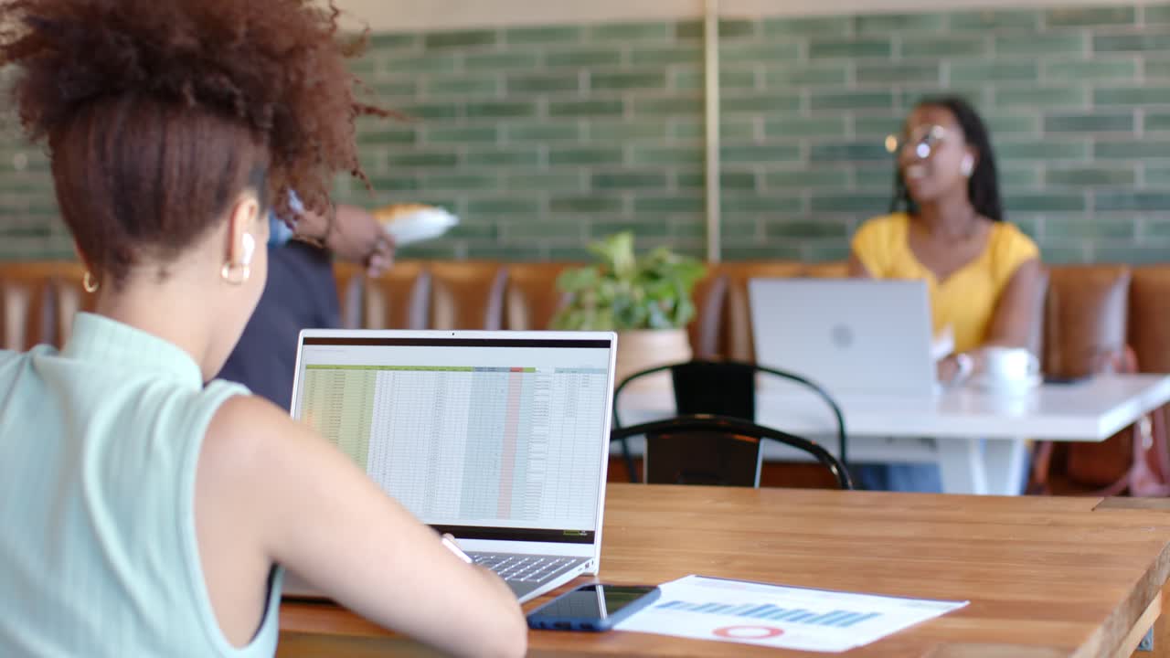 African American women in cafe left woman typing sheet glancing server bringing booth woman's plate
