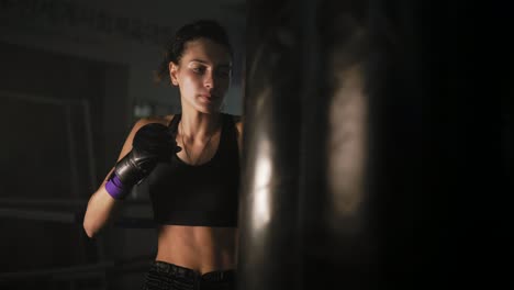 Schöne-Kickboxerin,-Die-Beim-Training-In-Einem-Dunklen-Fitnessstudio-Mit-Faust-Und-Ellenbogen-Boxsack-Schlägt.-Hartes-Training-Einer-Boxerin.-In-4k-Gedreht