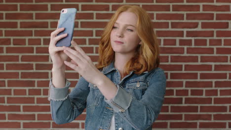 retrato de una hermosa mujer de cabello rojo usando un teléfono inteligente posando para una foto selfie