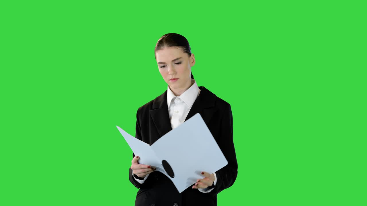 Young woman in office suit is getting ready to perform, looking into document on a Green Screen, Chroma Key