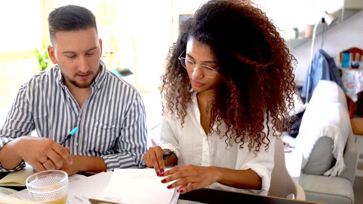 Coppia multietnica di freelance sorridenti che lavora insieme a casa