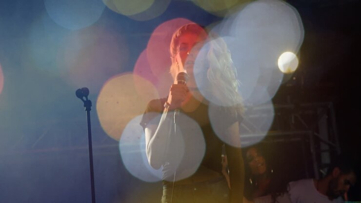 Cantante donna che tiene un microfono e canta su un palco musicale, con luci bokeh colorate animate.