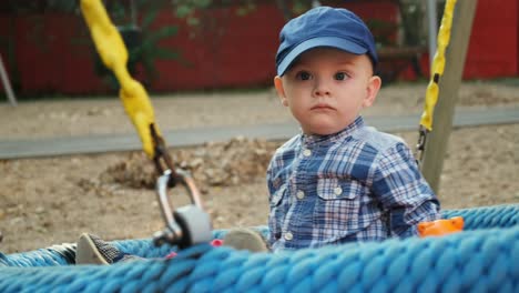 toddler boy swings on a round swing on the playground