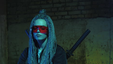 girl with dreadlocks and katanas in red glasses posing against a neon brick wall