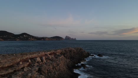 Vista-Por-Drones-De-Un-Acantilado-Sobre-El-Mar-Con-El-Increíble-Fondo-De-La-Isla-De-Es-Vedrá-En-Ibiza