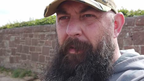 bearded urban man wearing baseball cap pondering looking across windy beach