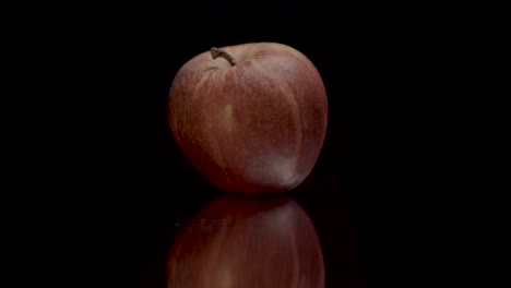 seguimiento lento en la manzana revelando en primer plano cinematográfico la textura y el color de la piel a medida que se enfoca contra el fondo negro y la superficie espejada