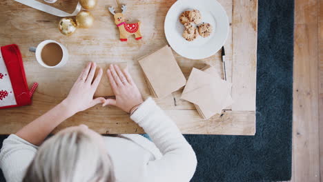 Ein-Blick-Von-Oben-Auf-Eine-Frau,-Die-Zu-Hause-Weihnachtskarten-Auf-Den-Tisch-Schreibt