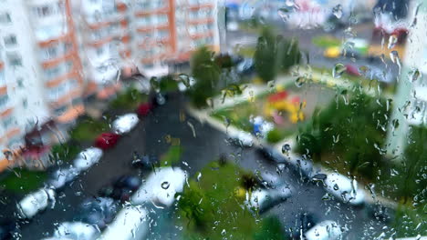 view on the yard in residential area through the window covered with rain drops. sight of the street from high rise floor of multistoried building.