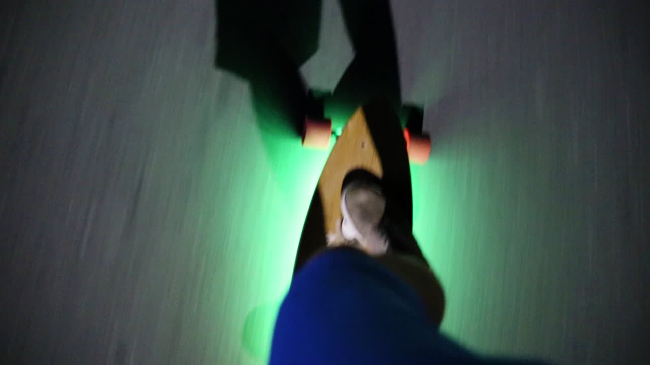 POV of riding skateboard with neon lights underneath at night in street. Handheld shot
