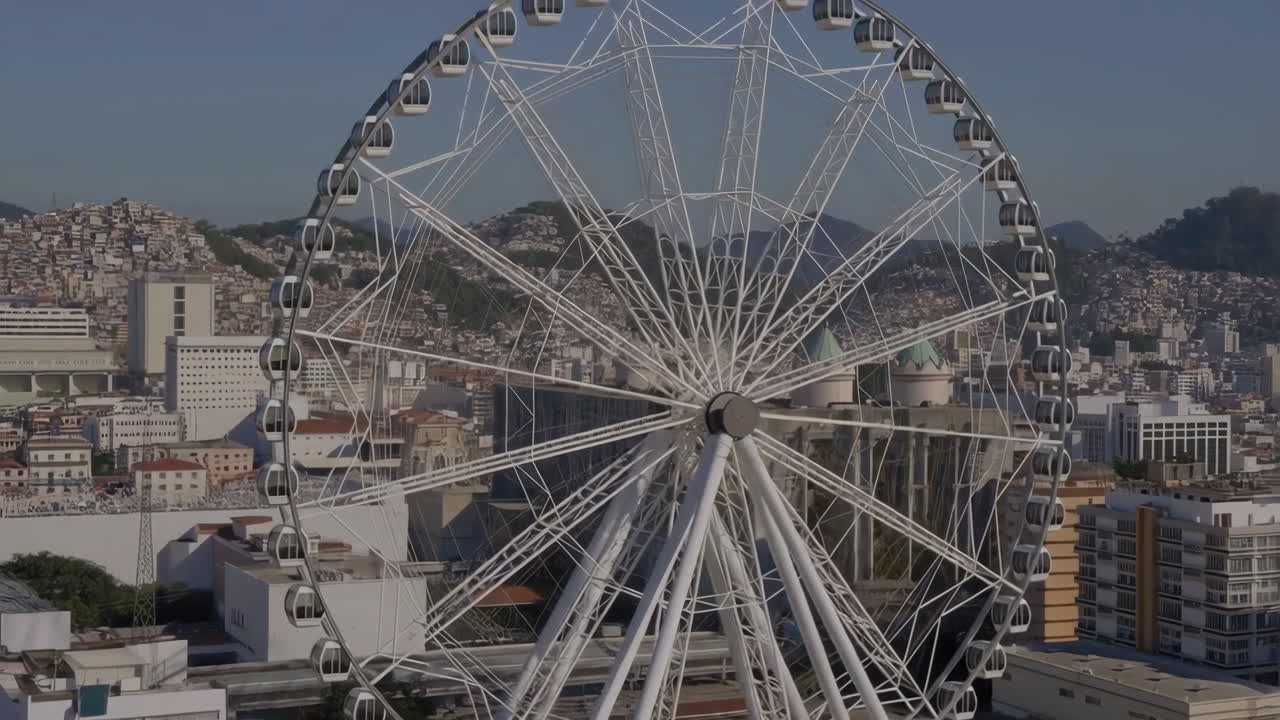 A large white Ferris wheel dominates a city skyline with distant hills under a clear sky