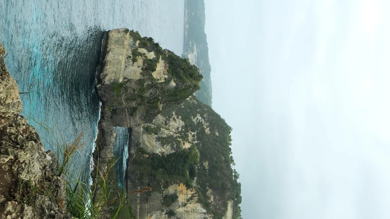 Vertical dolly forward reveal shot of Diamond Beach on Nusa Penida, Bali, from the cliffs above revealing a white sand beach and slow rolling swells