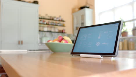 Close-up-of-tablet-with-smart-home-on-screen-over-fruit-in-bowl-in-kitchen,-slow-motion