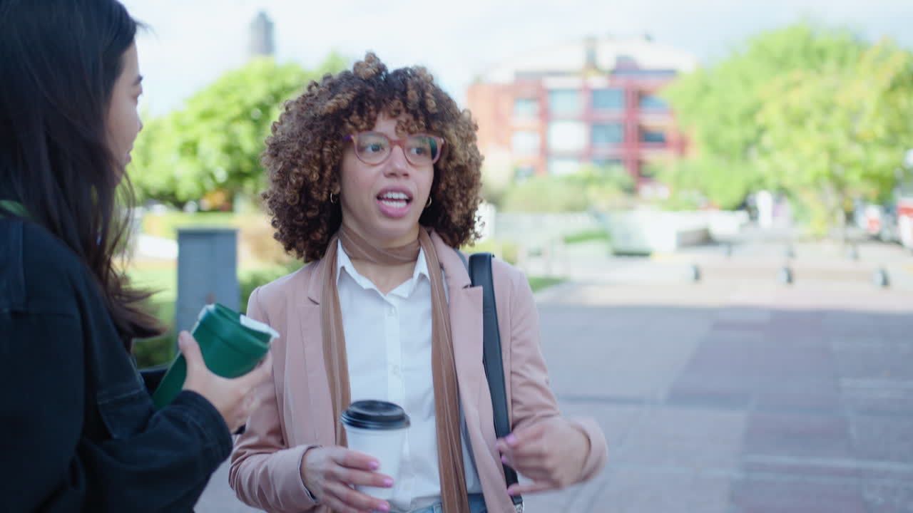 Young Black Woman Talking with Female Friend and Having Coffee Outdoors