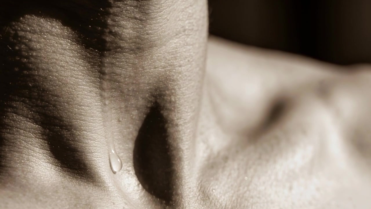 Sliding close-up neck and chest showing droplet sliding down hollow from breath, sepia light