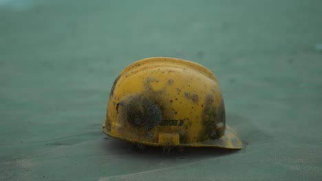 a weathered and moss-covered yellow hard hat lies abandoned on a sandy beach