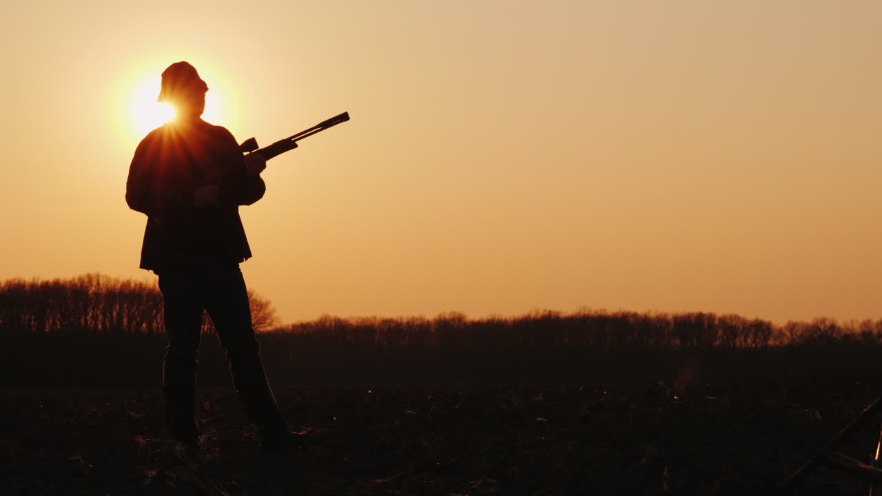 총을 든 사냥꾼의 실루엣 태양 광선이 그의 얼굴에 빛난다