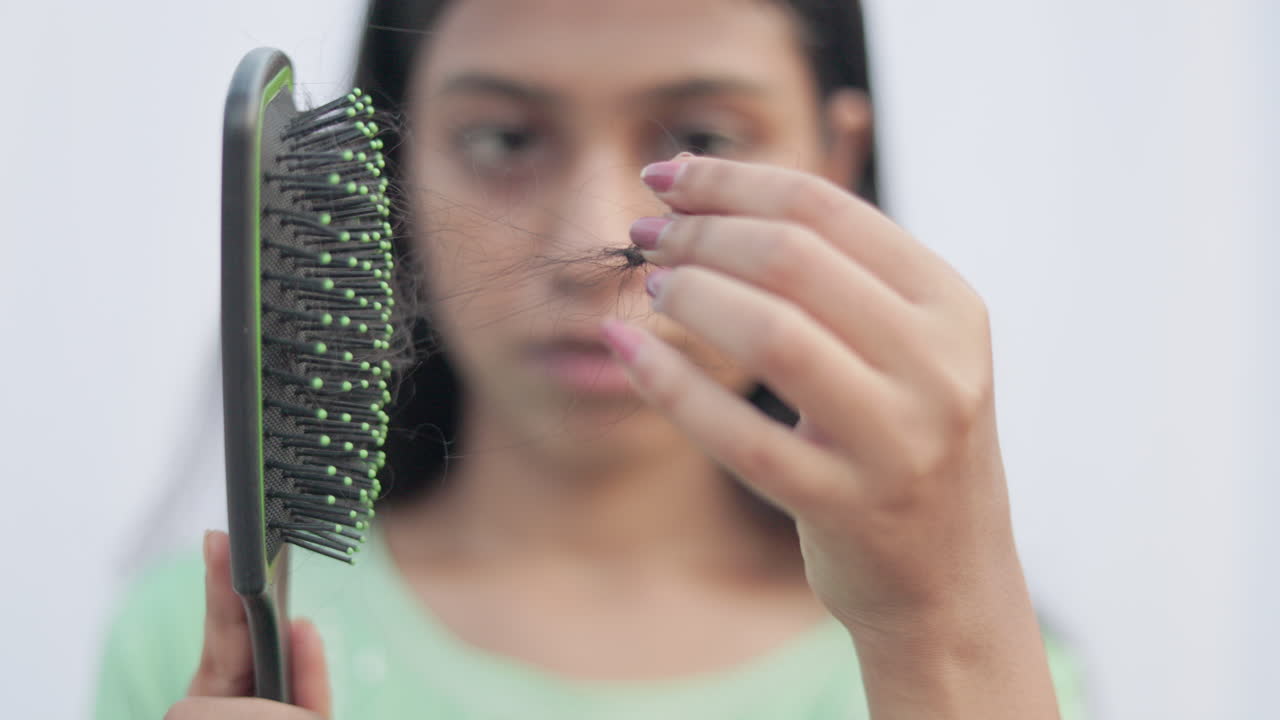 In white background a young lady taking out fallen hair from the brush with shocking face expression, focus on the comb.