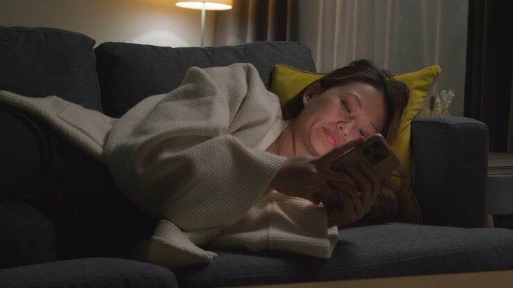 Woman Spending Evening At Home Lying On Sofa With Mobile Phone Scrolling Through Internet Or Social Media 4