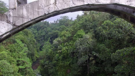 drone flying backwards under the bridge in indonesian jungle rainforest on bali island at cloudy weather