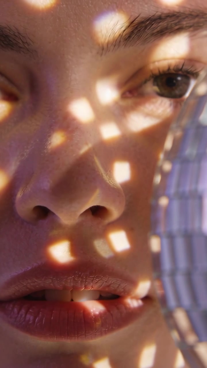 Rosto imóvel enquanto uma bola de espelhos entra e projeta reflexos em movimento para intensificar a luz.