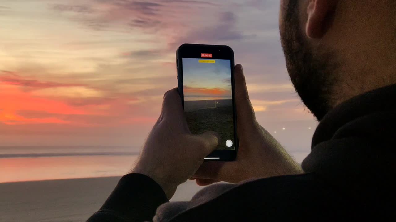 un joven turista graba un video de la puesta de sol en la playa con un teléfono inteligente moderno