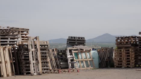 panning shot of columns of pallets piled vertically outdoors. different colours and sizes. some organized others not. horizon behind. mountains on skyline