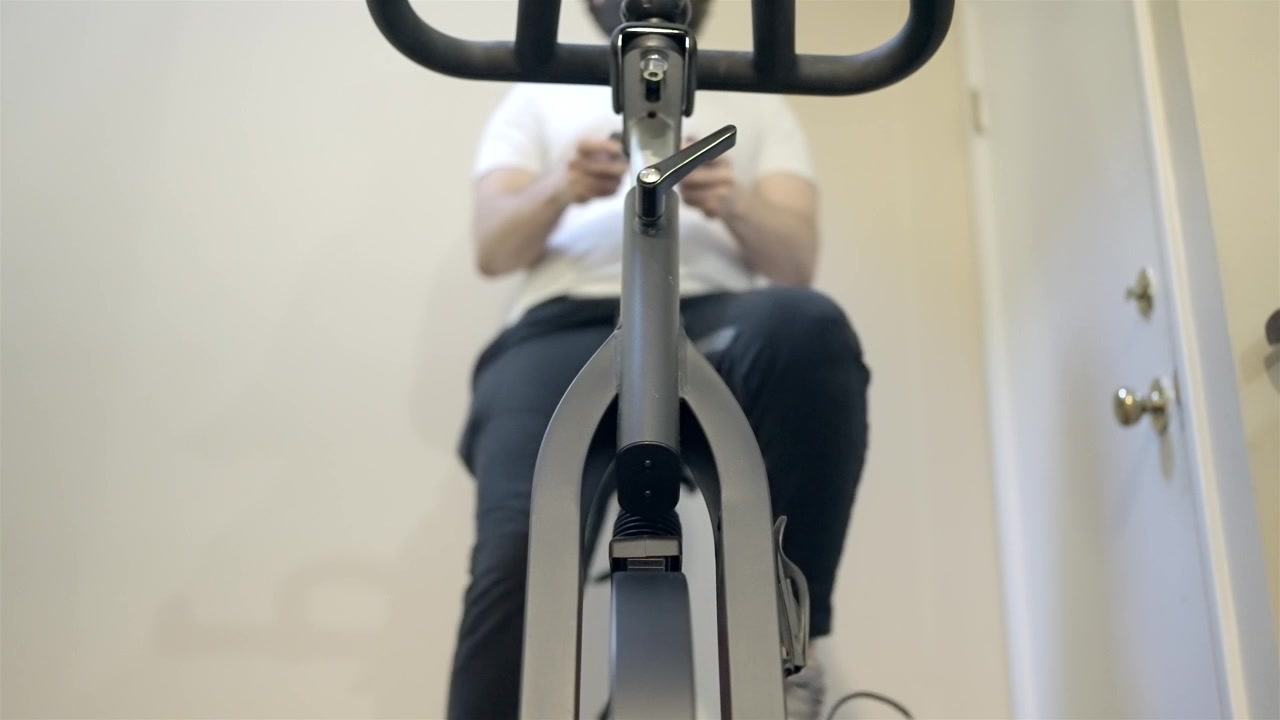 Persona haciendo ejercicio pedaleando en bicicleta de spinning en casa, sin rostro visible.