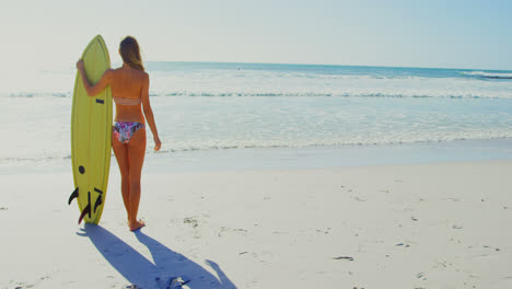 Rear-view-of-young-Caucasian-woman-standing-with-surfboard-on-the-beach-4k