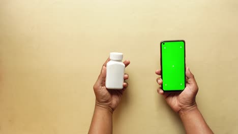 una persona sostiene una botella blanca y un teléfono con una pantalla verde.