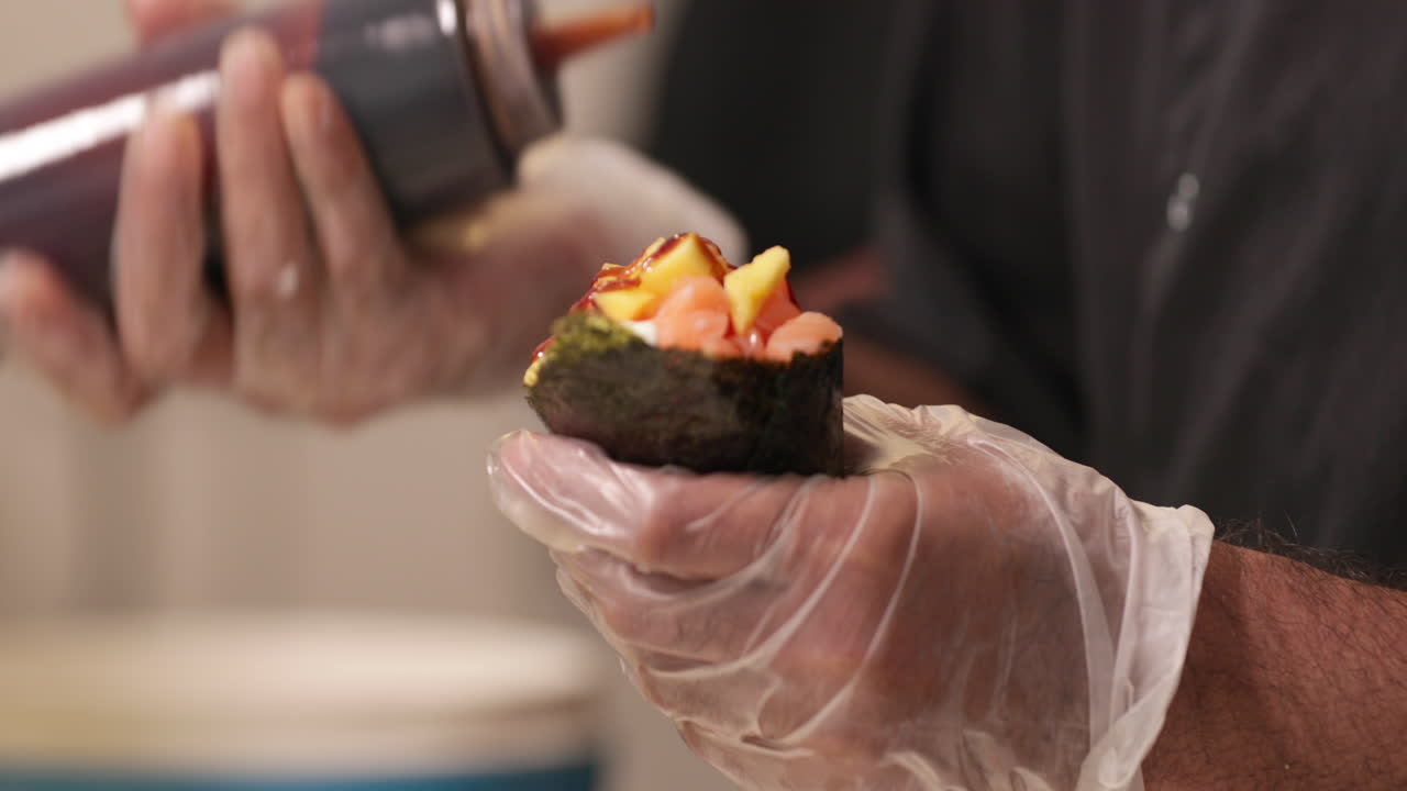chef con guantes sosteniendo un cono de sushi o un rollo de mano y poniendo salsa y cebolla antes de servir