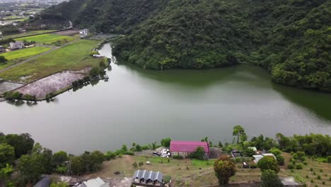 lago de agua verde en la base de una montaña verde y exuberante cerca de viviendas rurales y arrozales