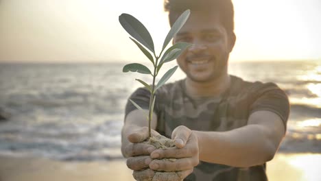 young man holding a small green plant or sampling in his both hands