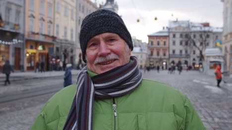 Stylish-old-senior-man-tourist-smiling,-showing-thumbs-up-in-winter-city-center-of-Lviv,-Ukraine