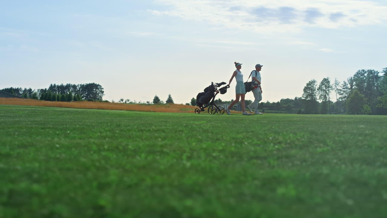 Golf players walk field on course. Golfing couple hold equipment clubs outside.