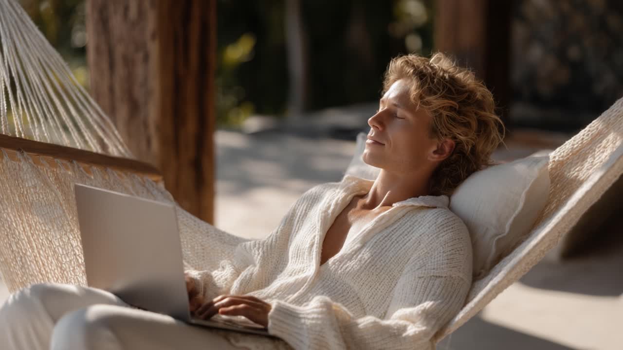 Serene Moment: A Relaxed Individual Enjoying Leisure Time on a Hammock While Using a Laptop in a Warm, Sunlit Outdoor Space
