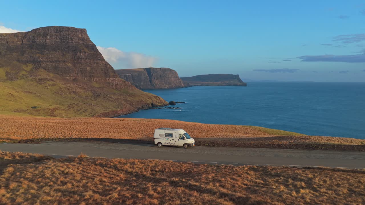 White camper van driving along scottish coastline road in the isle of skye