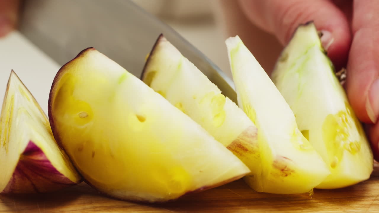 Close-Up of Hands Slicing a Yellow and Purple Tomato on a Cutting Board