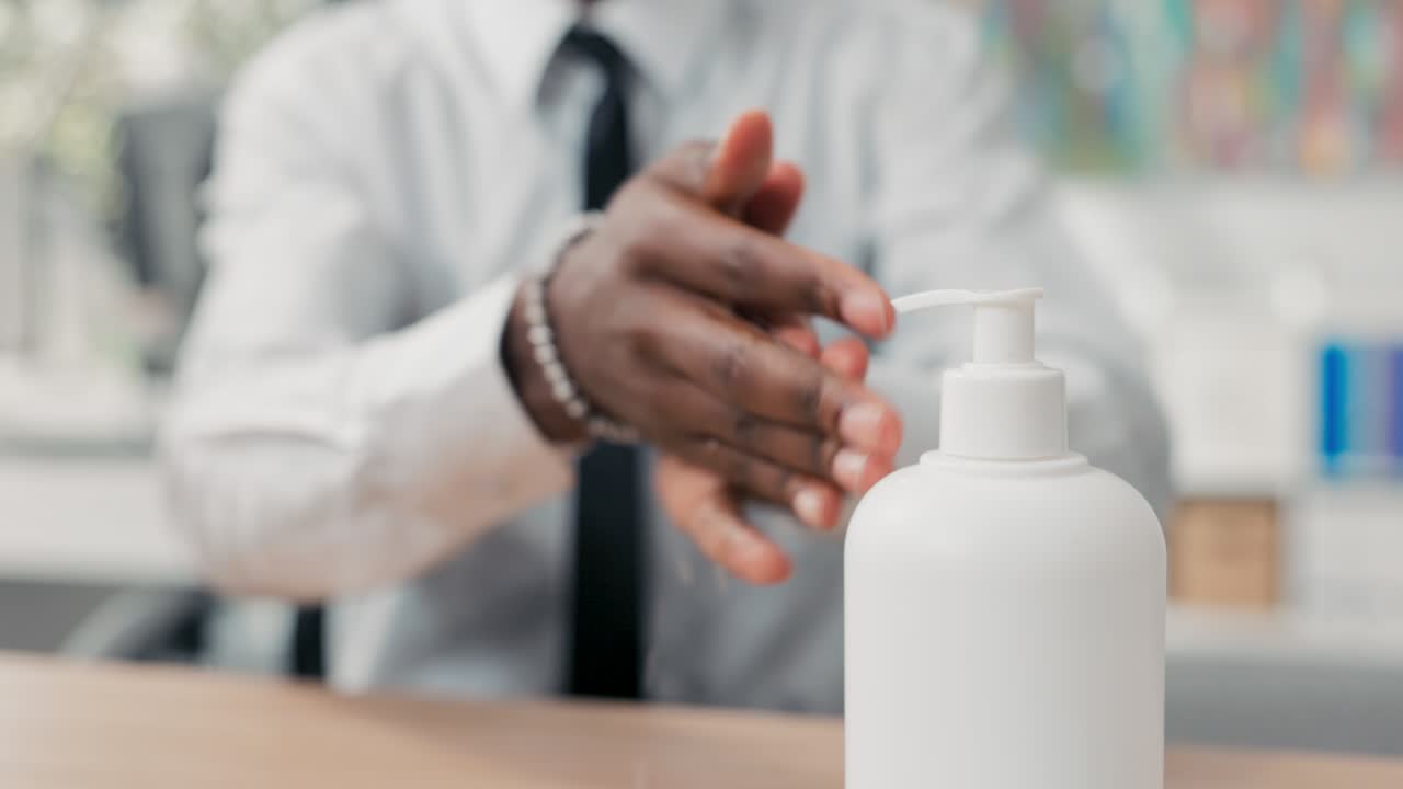 Hombre con camisa blanca y corbata aplica líquido de un dispensador, desinfecta sus manos antes de tocar el teclado de la computadora, higiene y seguridad en la oficina.