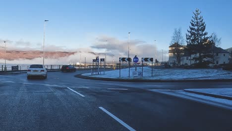 Snow-dusted-Glencoe-village-with-vehicles-and-quaint-houses,-clear-blue-sky,-car-POV