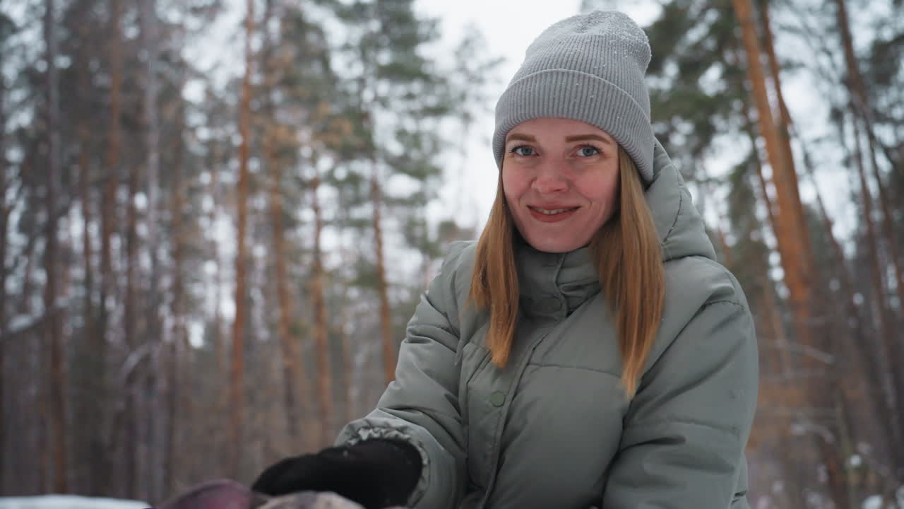 Smiling woman in gray winter coat and knit beanie posing in snowy pine forest, enjoying cold season outdoors, surrounded by tall trees and soft snow, expressing warmth, contentment, and winter spirit