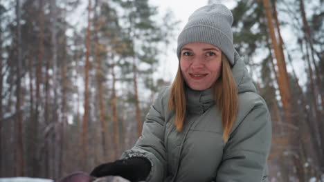 smiling woman in gray winter coat and knit beanie posing in snowy pine forest, enjoying cold season outdoors, surrounded by tall trees and soft snow, expressing warmth, contentment, and winter spirit