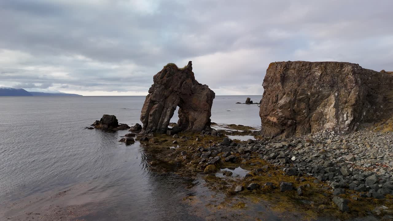 Aerial approaching shot of Gatanof seastack in Iceland during cloudy day. Seascape along coastline. Wide shot.