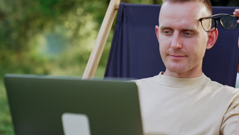 puzzled man looks at laptop screen waving head disapprovingly. freelancer working outdoors having some difficulties in work.