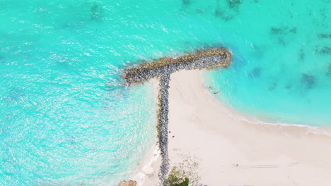 una toma aérea estática capturando una formación rocosa en forma de t en una playa con agua azul clara