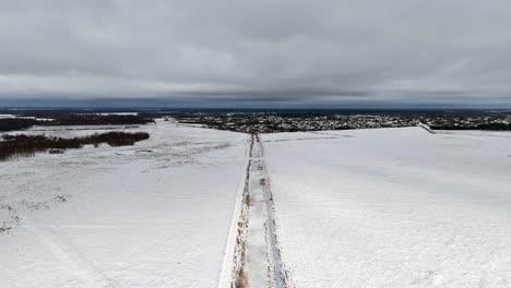 drone dolly along snow covered trench road leading to small city with dense clouds on horizon