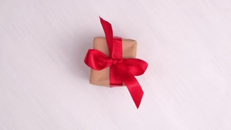 gift box with red ribbon spinning on pink wood background. 360 degree rotation. seamless loop. concept sales, discount price, christmas holidays and shopping