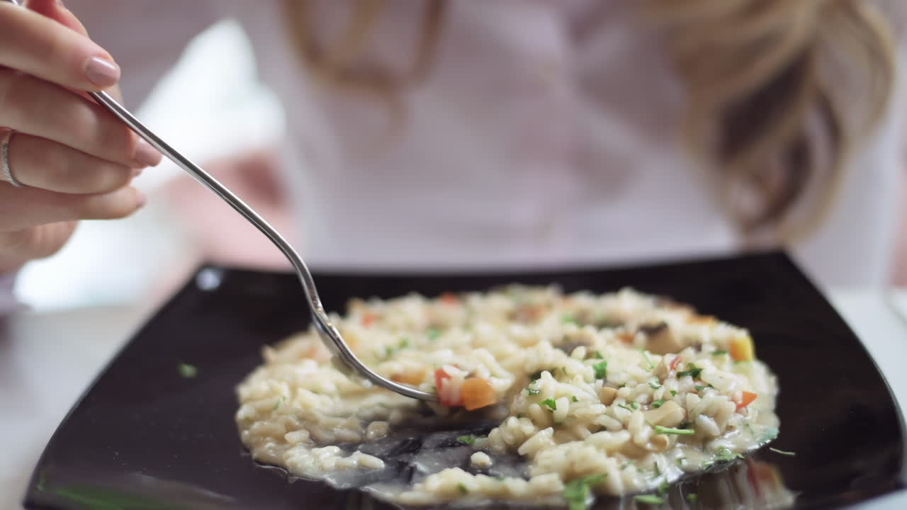 Close up of a woman eating risotto from a black plate at a restaurant