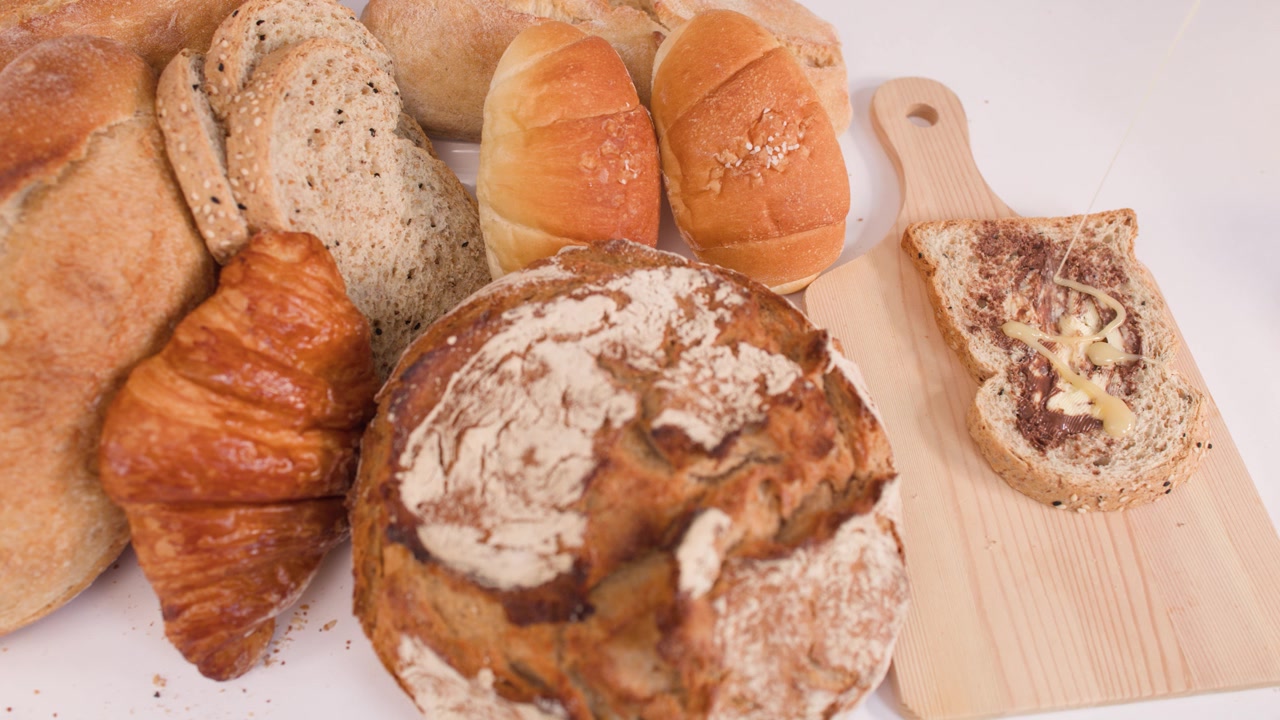 Overhead shot of sourdough, whole wheat toast, and croissants arranged on a wooden board.